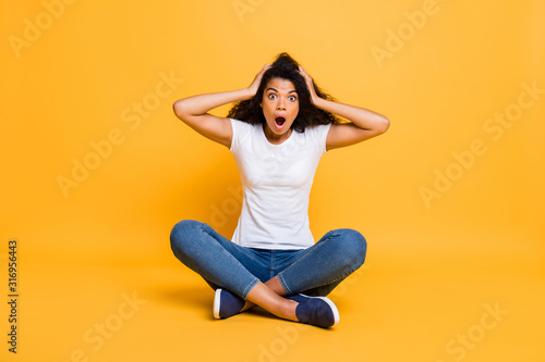 Full length body size photo of screaming shouting stunned curly wavy trendy stylish depressed youngster in jeans denim white t-shirt sitting on floor misunderstanding her failure isolated vivid yellow © deagreez