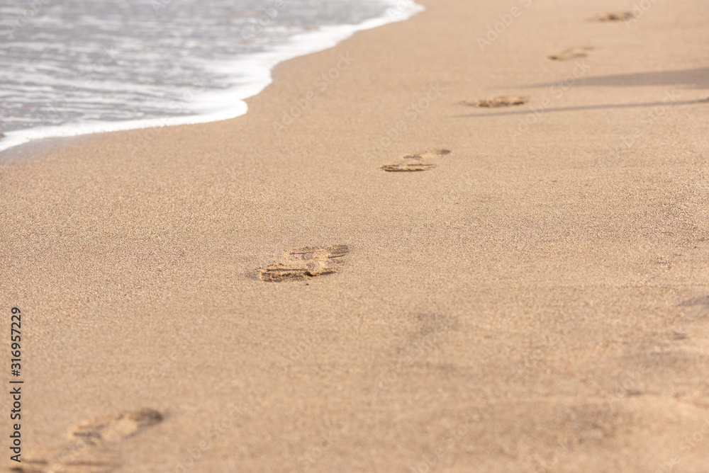 Footprints in the sand and wave with foam. The beautiful tourist's summer photo with wet sand, wave and footsteps. Footprints in the sand and wave with foam. The beautiful tourist's summer photo with wet sand, wave and footsteps.
