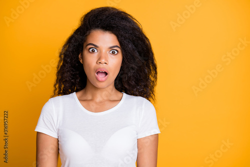 Photo of frightened stressed brown haired girl expressing fear on her face standing near empty space frightened with unexpected fail isolated over vivid color yellow background