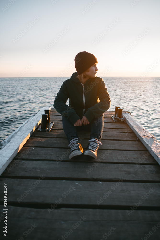 young traveling girl sits on a pier on the background of the sea and looks at the sunset young traveling girl sits on a pier on the background of the sea and looks at the sunset