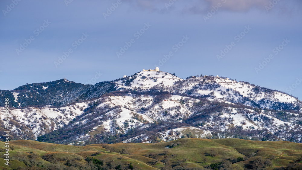 View towards the top of Mt Hamilton on a clear winter day, snow covering the summit and the surrounding hills; San Jose, San Francisco bay area, California