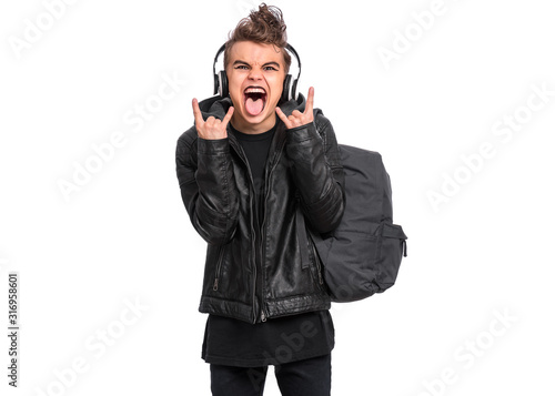 Crazy teen boy in headphones with spooking make-up making Rock Gesture, isolated on white background. Teenager with backpack, dressed in black screaming and shouting, doing heavy metal rock sign.