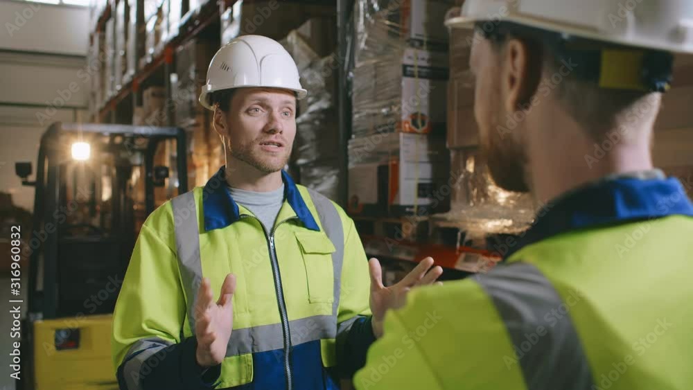 Warehouse workers talking together at work in a large warehouse Warehouse workers talking together at work in a large warehouse