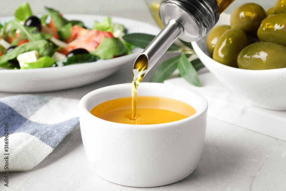 Pouring cooking oil into bowl on light grey marble table Pouring cooking oil into bowl on light grey marble table