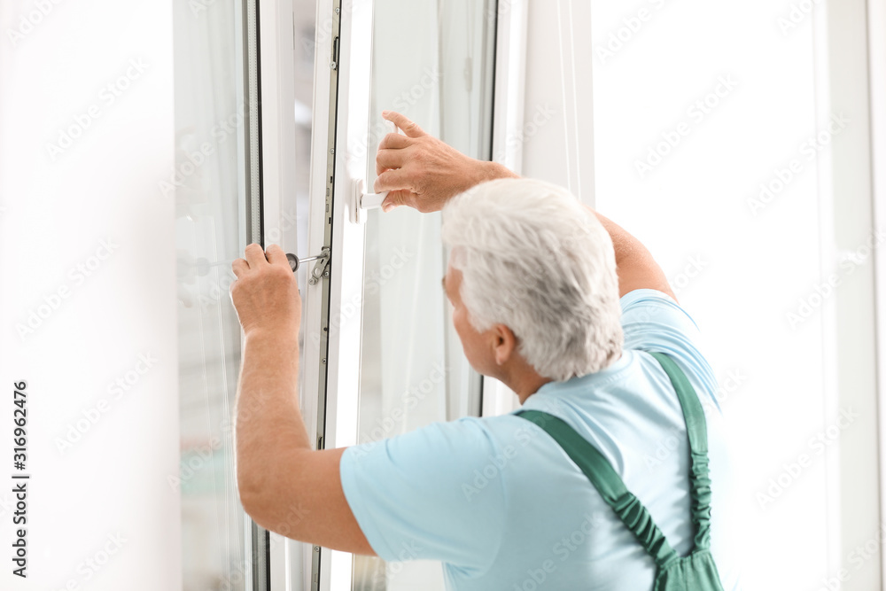 Mature construction worker repairing plastic window with screwdriver indoors