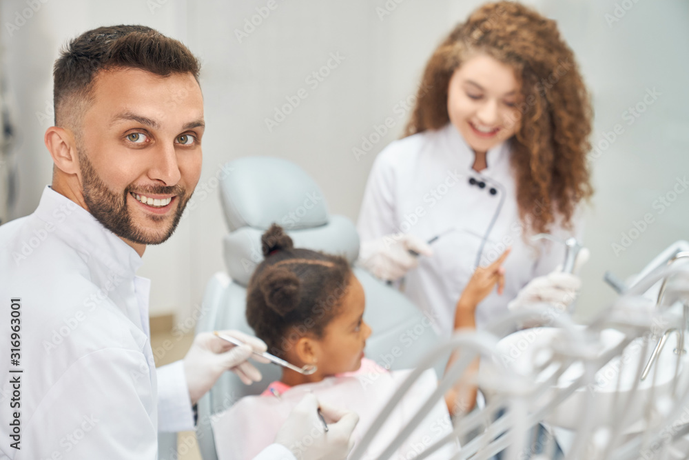 Fototapeta premium Afro girl in dental chair with dentist and assistant around