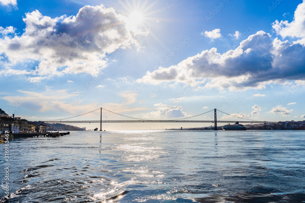 25th of April bridge over the river Tagus estuary with sun star and dramatic clouds in Lisbon, Portugal