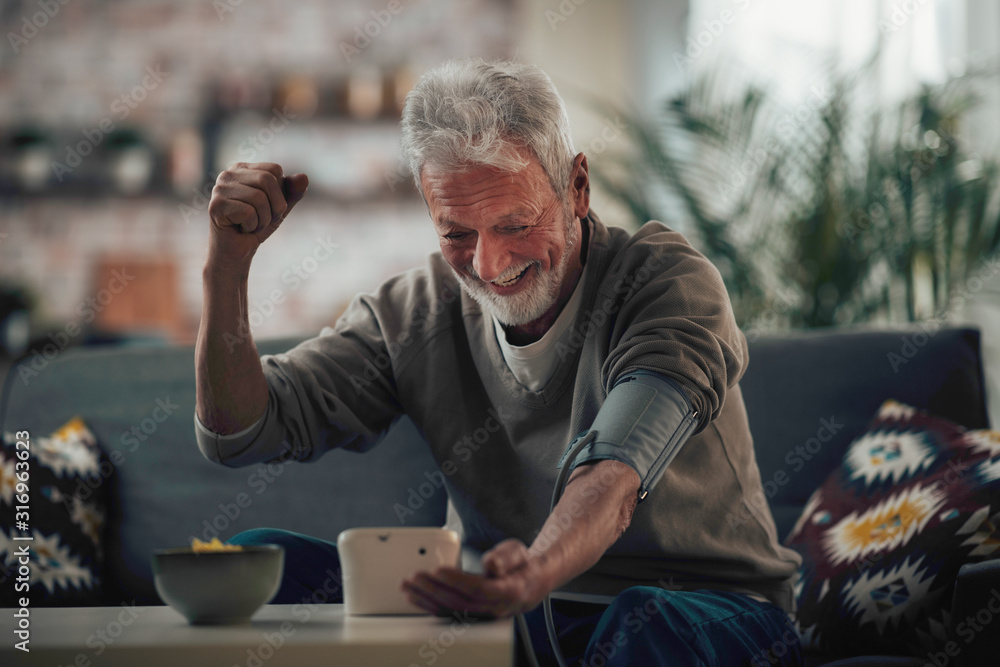Old man sitting in living room. Happy senior man checking blood pressure. Old man sitting in living room. Happy senior man checking blood pressure.
