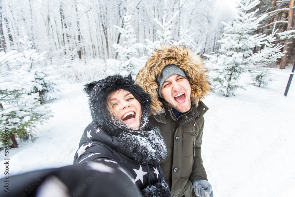 Season, love, technology and leisure concept - happy couple taking selfie by smartphone over winter background