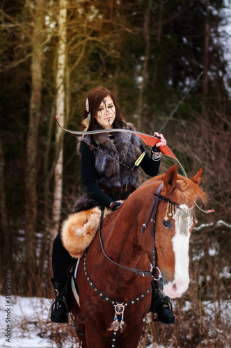 a Viking girl riding a red horse painted in black runes. holds a bow and shoots it