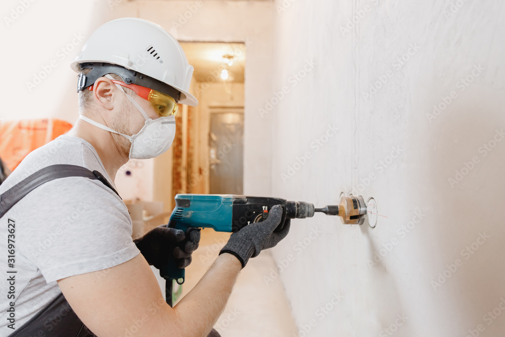 Builder worker pneumatic hammer drills hole in concrete brick wall with diamond crown for electric cable, socket, switch Builder worker pneumatic hammer drills hole in concrete brick wall with diamond crown for electric cable, socket, switch