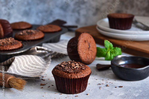 Chocolate muffins with chocolate moss sauce and mint on a concrete background.