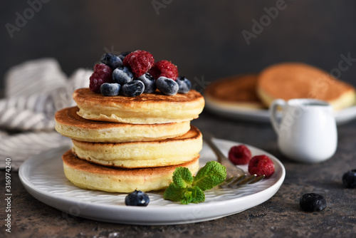 Beautiful pancakes with berries and sauce on a dark concrete background.