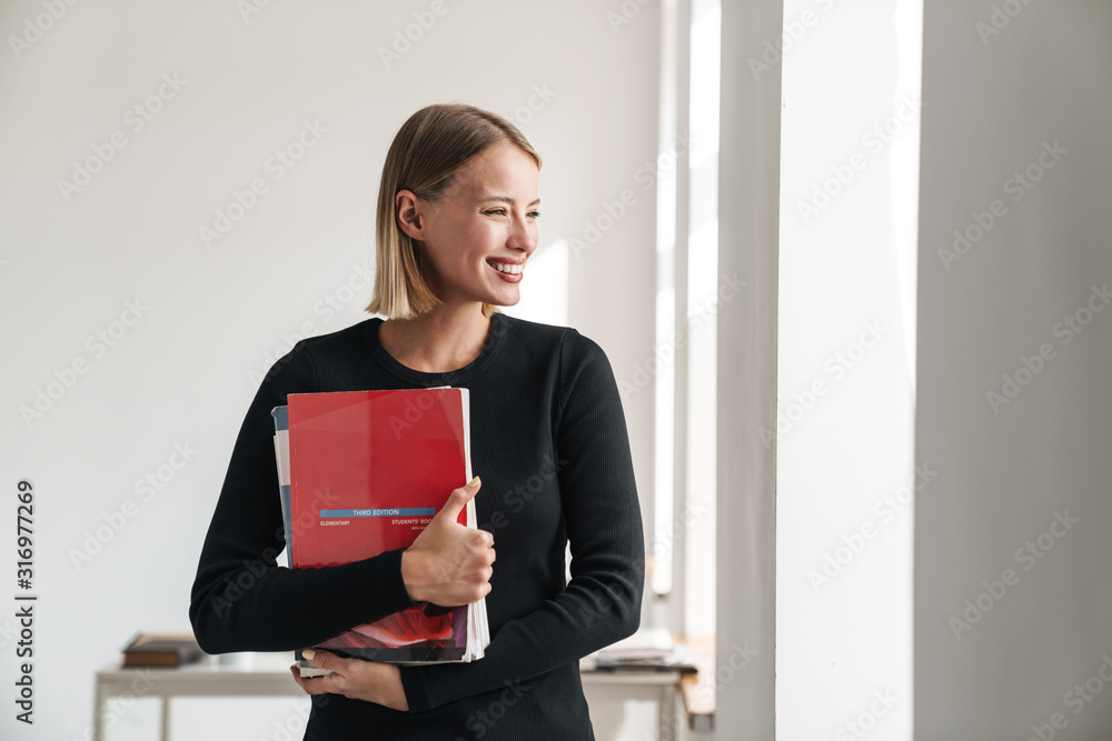 Blonde woman student indoors holding copybooks.