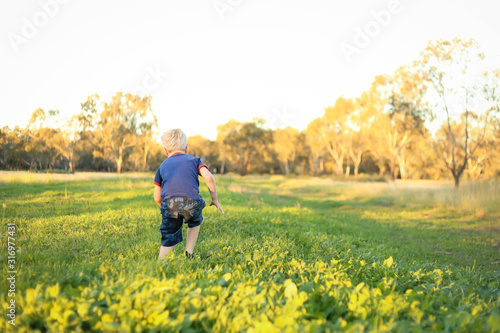 Little boy running away from camera through lush green grass in a vibrant field at sunset with copy space