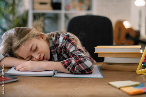 Tired schoolgirl sleeping on desk. Cute girl fell a sleep while studying. 
