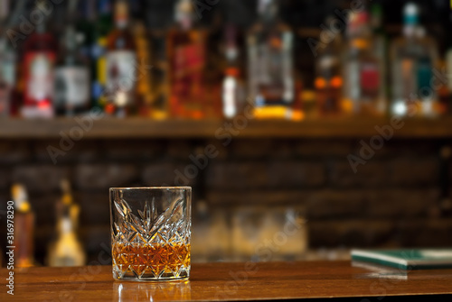 Yellow cocktail on bar counter. Whiskey, rum or brandy on the background of bottles with alcohol. Glass with booze on a wooden board.