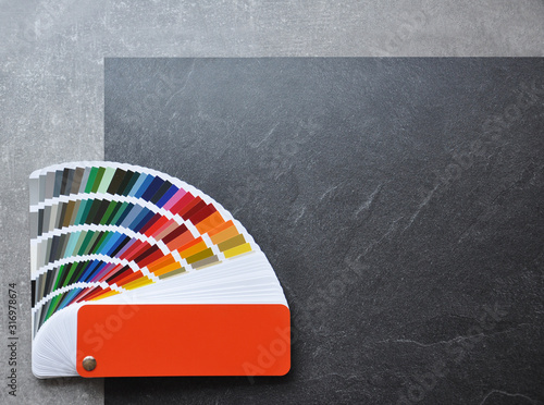 Color palette guide, fan, catalogue on grey and black background. Ral color fan  with orange cover on conсrete texture photo