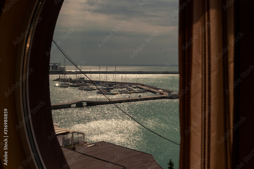 Room with a round window view over the docks with small boats on the coast of the Black Sea.