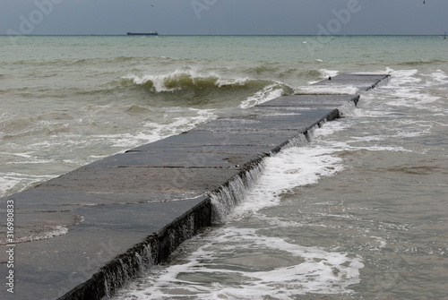 Concrete pier on the Black Sea washed away by the agitated waves with a distant vessel sitting on the horizon.