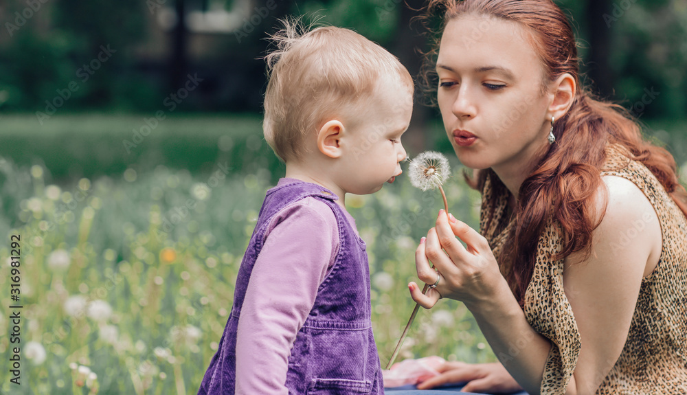 young mom with her little daughter blowing on a dandelion