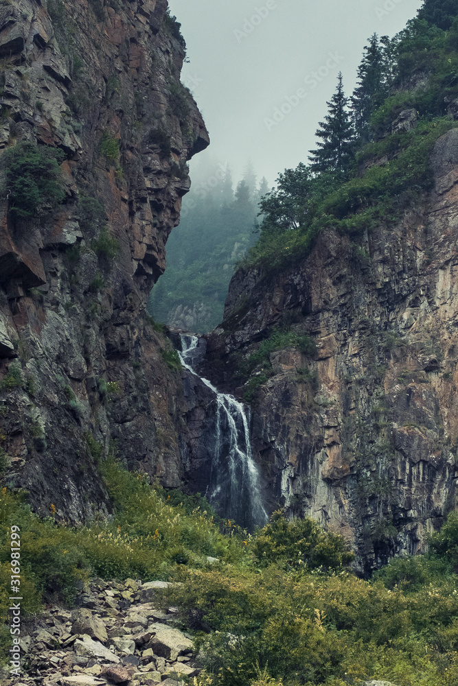 Obraz premium Butakovsky waterfall in rocks and fog in the mountains of Zailiysky Alatau in the city of Almaty Kazakhstan