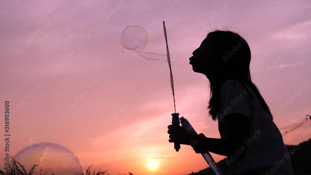 Little girl playing with bubbles in the park at sun set.