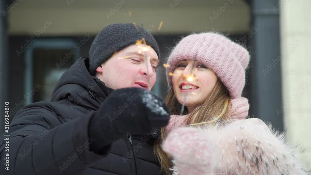 Young Romantic Couple Holding Bengal Lights Sparklers in Winter day. They Kissing and Smiling. Slow Motion. Lifestyle, Love, Dating, Romantic Relationships and Valentines Day Concept Young Romantic Couple Holding Bengal Lights Sparklers in Winter day. They Kissing and Smiling. Slow Motion. Lifestyle, Love, Dating, Romantic Relationships and Valentines Day Concept