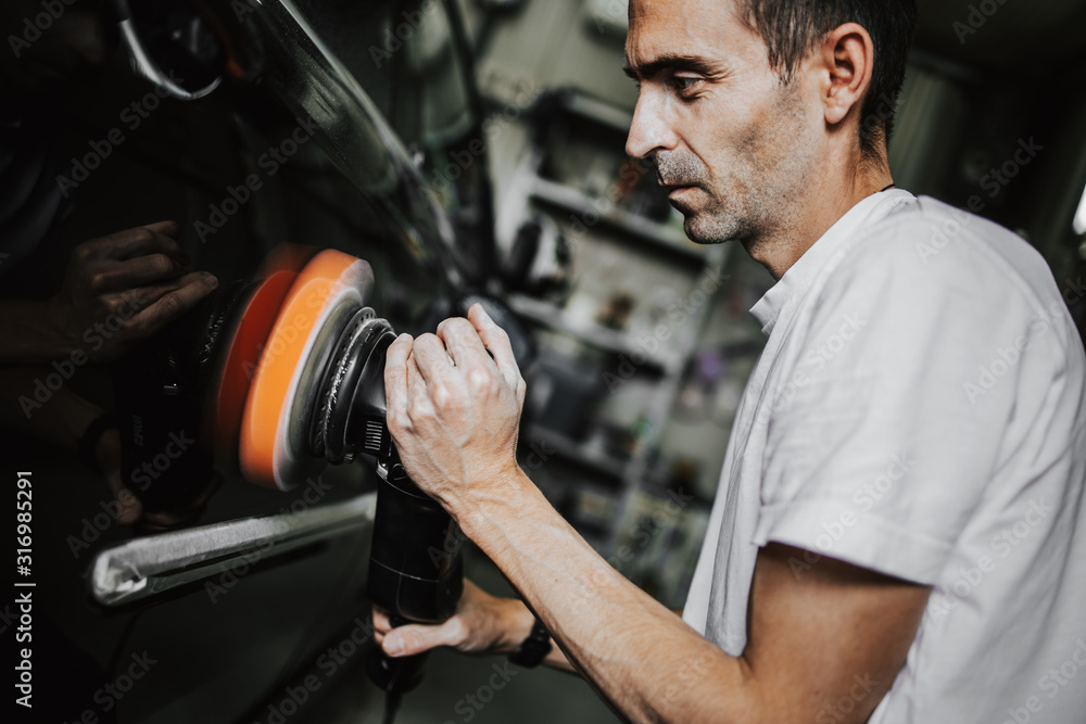 Car detailing - Hands with orbital polisher in auto repair shop. Selective focus. Old film color grade. Car detailing - Hands with orbital polisher in auto repair shop. Selective focus. Old film color grade.