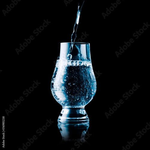 Liquid poured into a glas - blue toned isolated on black
