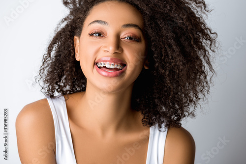 Schilderij op canvas laughing african american girl with dental braces, isolated on grey