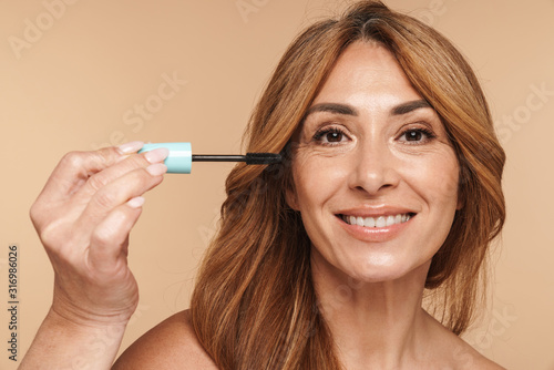 Portrait of shirtless adult woman applying mascara and smiling