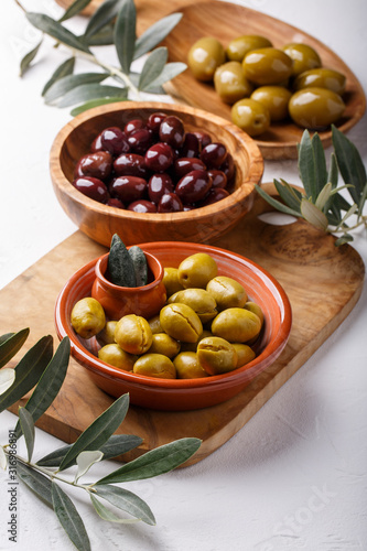 Different types of olives green and black in bowls on white table.