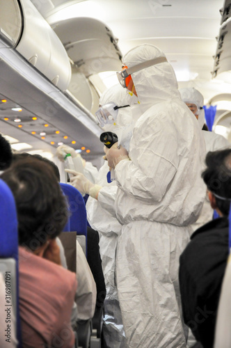Medics in white hazmat protective suits checking and scanning passengers in a plane for epidemic virus symptoms. Chinese new Wuhan coronavirus illustration.