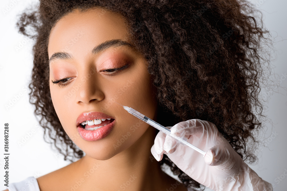 Fototapeta premium beautiful young african american woman making beauty injection, isolated on grey