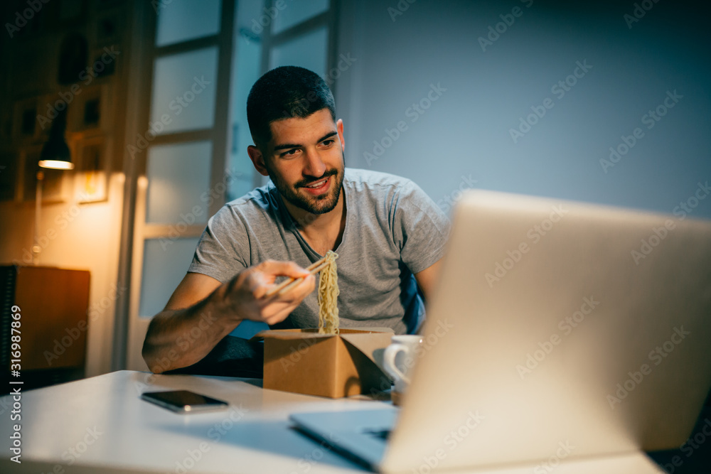 man at home eating chinese food and using laptop man at home eating chinese food and using laptop