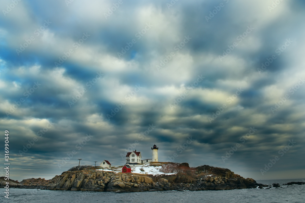 Lighthouse on an island in the Atlantic Ocean and fantasy striped clouds.  New Harbor. USA