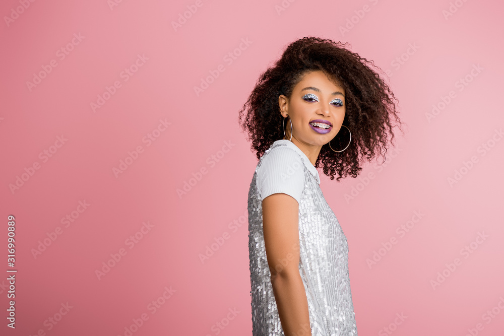 cheerful stylish african american girl with dental braces, with silver glitter eyeshadows and purple lips dancing in paillettes dress, isolated on pink cheerful stylish african american girl with dental braces, with silver glitter eyeshadows and purple lips dancing in paillettes dress, isolated on pink