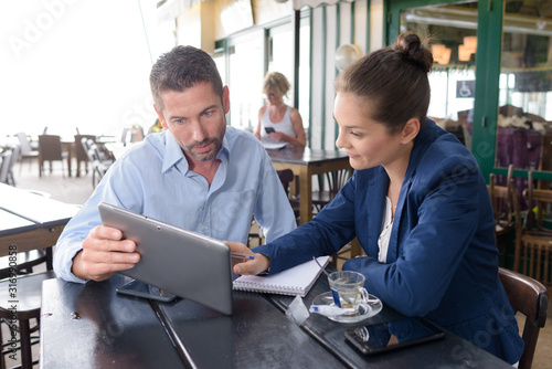 man and woman meeting in cafe looking at tablet pc