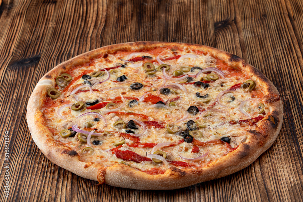 Italian pizza with red onion, black and green olives, melted cheese and ketchup on rustic textured background