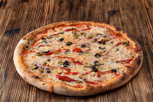 Italian pizza with red onion, black and green olives, melted cheese and ketchup on rustic textured background