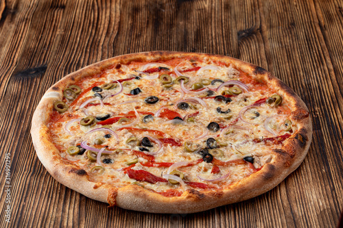 Italian pizza with red onion, black and green olives, melted cheese and ketchup on rustic textured background