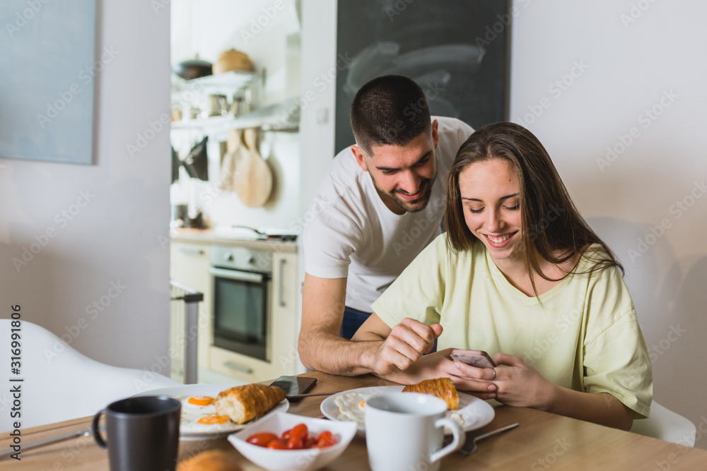 happy couple using smartphone while having breakfast at home
