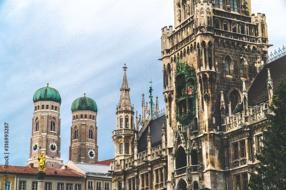 Fototapeta premium The New Town Hall, Neues Rathaus on Marienplatz main square, city government building with a tower clock. Gothic style. Photographed from below. Wide shot with Munich Frauenkirche in background. Wide 