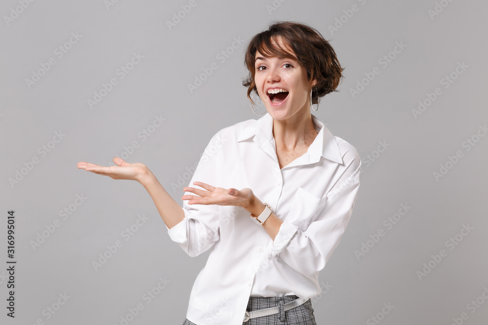 Excited cheerful young business woman in white shirt posing isolated on grey wall background, studio portrait. Achievement career wealth business concept. Mock up copy space. Pointing hands aside. Excited cheerful young business woman in white shirt posing isolated on grey wall background, studio portrait. Achievement career wealth business concept. Mock up copy space. Pointing hands aside.
