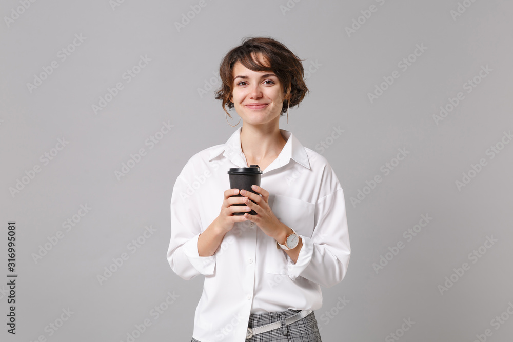Smiling young business woman in white shirt posing isolated on grey wall background studio portrait. Achievement career wealth business concept. Mock up copy space. Holding paper cup of coffee or tea. Smiling young business woman in white shirt posing isolated on grey wall background studio portrait. Achievement career wealth business concept. Mock up copy space. Holding paper cup of coffee or tea.