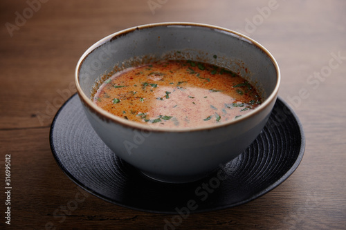Tomato soup with herbs in a ceramic plate on a dark wooden table.