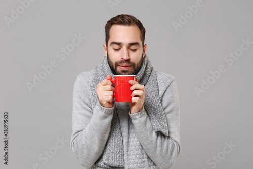 Konstfotografi Frozen young man in gray sweater, scarf posing isolated on grey wall background, studio portrait