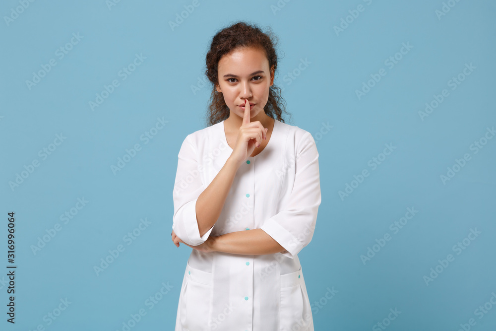 African american doctor woman isolated on blue background. Doctor in medical gown say hush be quiet with finger on lips shhh gesture. Healthcare personnel health medicine concept. Mock up copy space. African american doctor woman isolated on blue background. Doctor in medical gown say hush be quiet with finger on lips shhh gesture. Healthcare personnel health medicine concept. Mock up copy space.