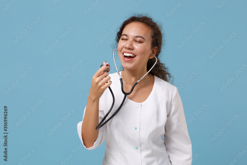 Cheerful african american doctor woman isolated on blue background studio portrait. Female doctor in medical gown using stethoscope. Healthcare personnel medicine health concept. Mock up copy space. Cheerful african american doctor woman isolated on blue background studio portrait. Female doctor in medical gown using stethoscope. Healthcare personnel medicine health concept. Mock up copy space.